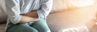 Woman sitting on couch holding stomach in discomfort.